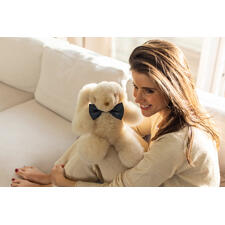 Alpaka-Hase - Flauschig fein und seidenzart. Kein Vergleich zu plüschigem Kunstfell. Frau hält einen kleinen, champagnerfarbenen Alpaka-Hasen mit schwarzer Schleife.