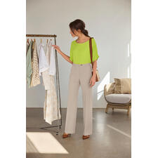 Limette Frau in einer hellgrünen T-Shirt-Bluse, steht neben einem Kleiderständer.