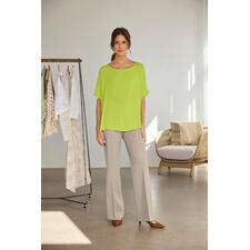 Limette Frau in einer limettengrünen T-Shirt-Bluse, steht lässig neben einem Kleiderständer.