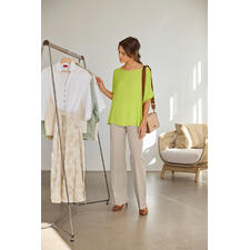 Limette Frau in einer hellgrünen T-Shirt-Bluse, betrachtet Kleidungsstücke am Kleiderständer.