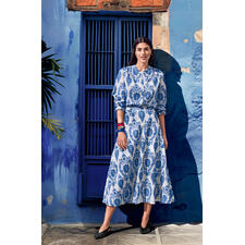 Rot, Gelb und Blau Frau in einem blauen Kleid mit weißem Muster, steht vor einer blauen Wand.