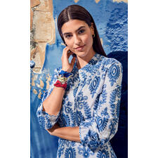 Rot, Gelb und Blau Nahaufnahme von einer Frau mit blauem Musterkleid, lächelt in die Kamera.