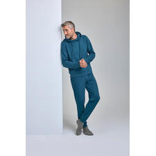 Cashmere Cotton Loungewear-Anzug Mann in tealfarbigem Cashmere-Cotton Loungewear-Anzug lehnt an Wand.