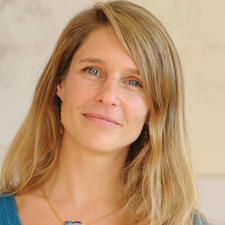 Sukhi Barber Portrait einer lächelnden Frau mit langen Haaren und blauen Augen, im Hintergrund unscharf.