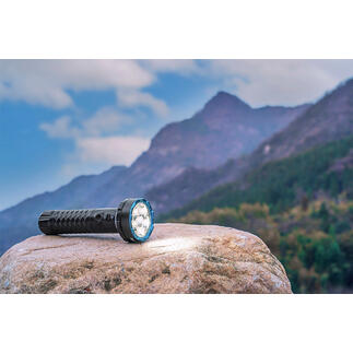 Bidirektionale 5.000 Lumen Taschenlampe auf einem Stein mit Berglandschaft im Hintergrund.
