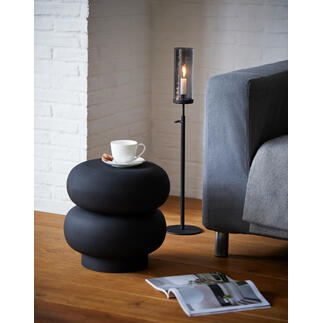 Höhenverstellbares Windlicht neben Sofa, auf schwarzem Beistelltisch mit Tasse und Zeitschrift.
