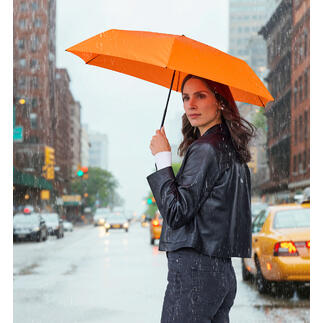 Frau hält einen orangen Taschenschirm in der Regen, auf der Straße stehend.