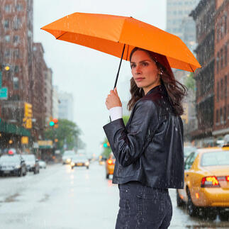 Frau hält einen orangen Taschenschirm in der Regen, auf der Straße stehend.