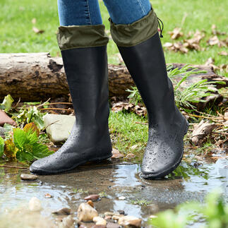 Schwarze Gummistiefel mit umgeschlagenem oberen Teil, stehen am Rand eines Wasserlaufes.