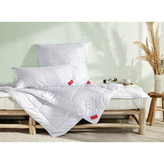 Bett mit weißen Kissen und einer Decke, helle Schlafzimmeratmosphäre.