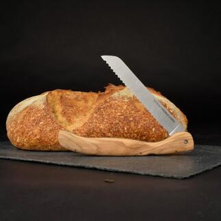 Klappbares Brotmesser mit Olivenholzgriff neben einem Laib Brot auf einer schwarzen Unterlage.