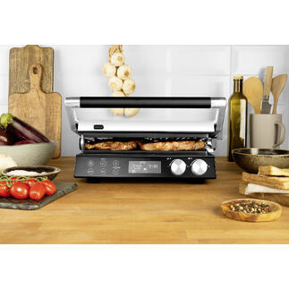 4-in-1 Multigrill auf einem Tisch mit gegrilltem Essen und frischen Zutaten.