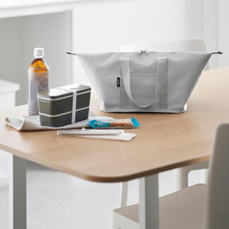 Hellgraue Vario-Kühltasche auf einem Tisch, umgeben von Snacks und Getränken.