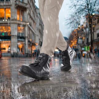 Person trägt schwarze Stiefel mit Silikon-Schuhüberziehern im Regen auf einer nassen Straße.