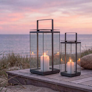 Zwei Design-Laternen auf einer Holzterrasse am Strand bei Sonnenuntergang.
