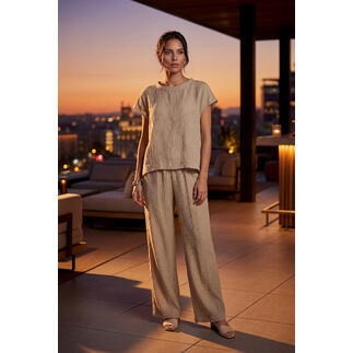 Frau trägt eine sandfarbene Bluse und weite Hose, im Abendlicht.
