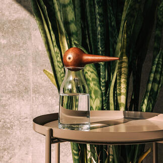 Glas wasser mit hölzernem Wasserspender in Form eines Vogels auf einem Tisch.