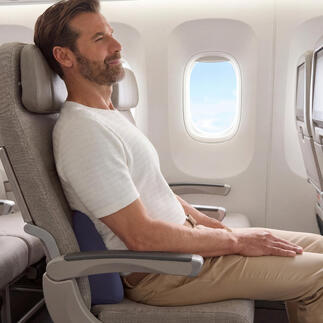 Mann sitzt im Flugzeug mit einem Reise-Rückenkissen zur Unterstützung des Rückens.