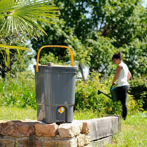 BioMix Flüssigdünger-Bereiter in einem Garten, im Hintergrund arbeitende Frau.