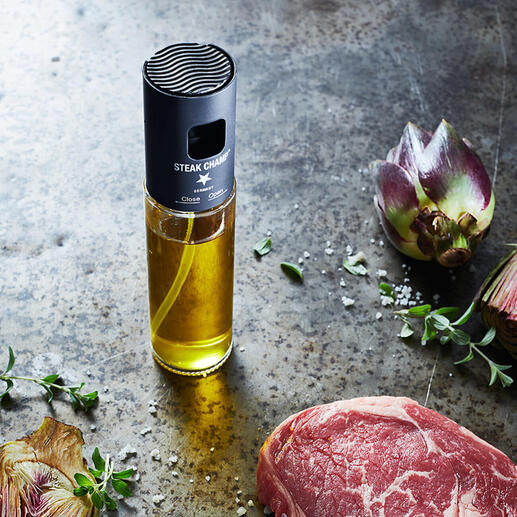 Öl-Zerstäuber mit Filter neben rohem Steak und Kunstblumen auf rustikalem Tisch.