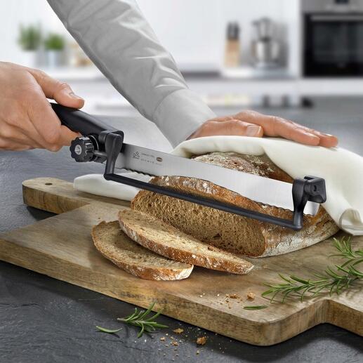 Hand schneidet Brot mit einem Sägemesser und einer Schnittführung auf einem Holzbrett.