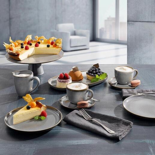 Geschirrserie mit verschiedenen Tellern, Tassen und Kuchen auf einem Tisch.