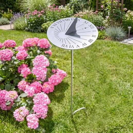 Edelstahl Sonnenuhr auf einem grünen Rasen, umgeben von pinken Blumen.