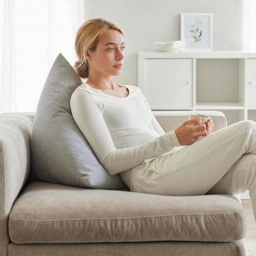 Frau mit einem grauen Rückenkissen, die entspannt auf einer Couch sitzt.