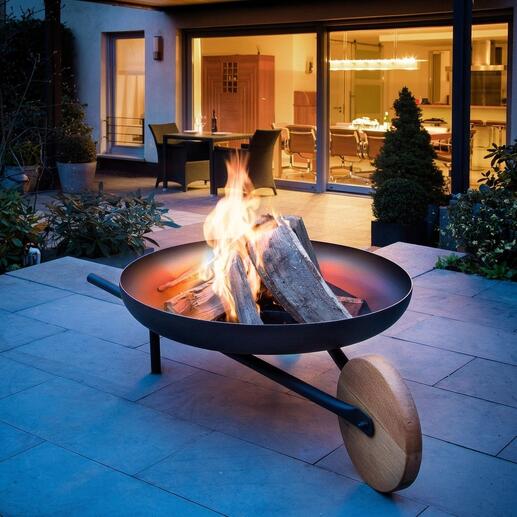 Feuerschale mit Grillfunktion, Flammen und Holzscheiten auf einer Terrasse.