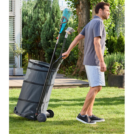 Mann zieht einen faltbaren Gartentrolley mit Laub durch den Garten.