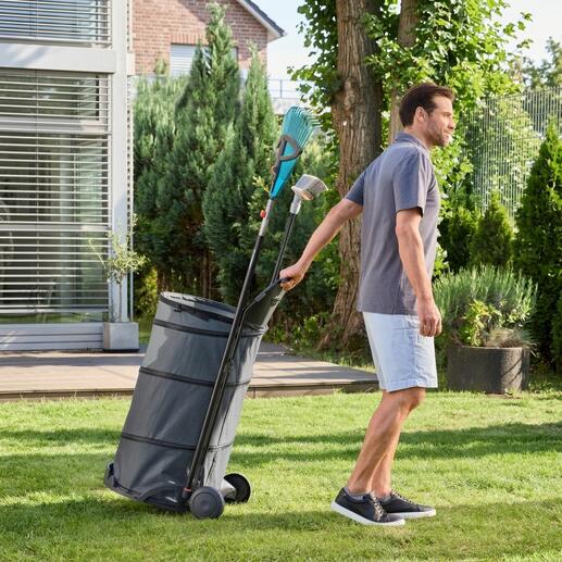 Mann zieht einen faltbaren Gartentrolley mit Laub durch den Garten.