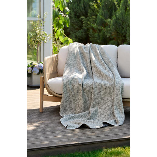 Umkehrbare jacquard Decke liegt auf einer Gartenbank.