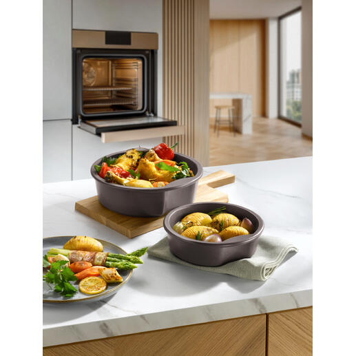 Zwei Keltentöpfe mit Gemüse und Kartoffeln auf einem Holzteller in moderner Kücheneinrichtung.