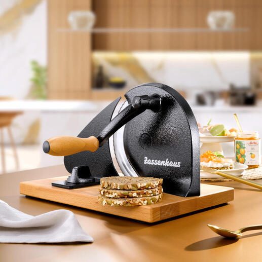 Handkurbel-Brotschneider auf einer Holzplatte mit frisch geschnittenem Brot.