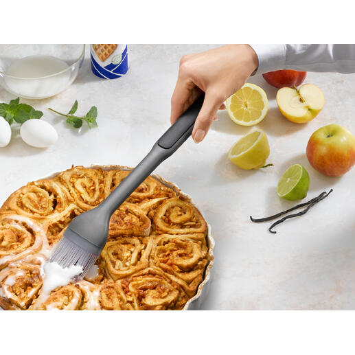 Hand mit einem Backpinsel, der einen warmen Zimtkuchen bestreicht.