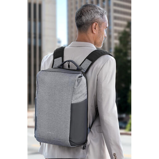 Mann mit grauem Anti-Diebstahl-Rucksack auf dem Rücken vor urbanem Hintergrund.