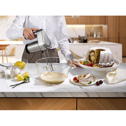 Mann hält Gastroback Power-Handmixer über einer Schüssel mit Teig und Kuchen auf einem Tisch.