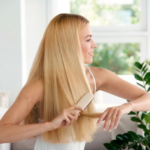 Frau mit blonden Haaren bürstet ihre Haare mit einer Haarbürste auf einem hellen Hintergrund.