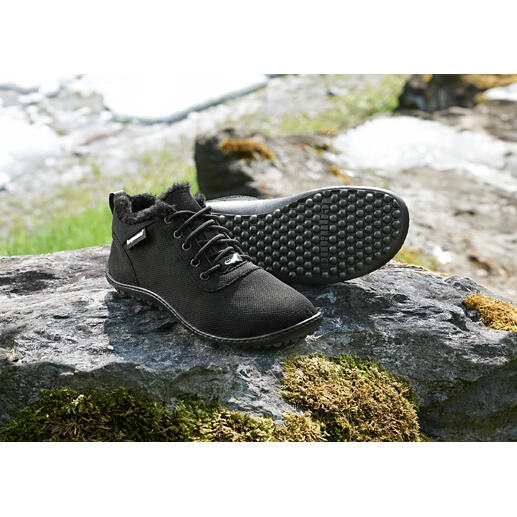 Schwarze Winter-Sneaker auf einem Stein mit Schneeresten im Hintergrund.