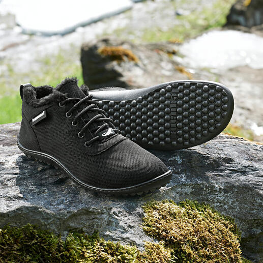 Schwarze Winter-Sneaker auf einem Stein mit Schneeresten im Hintergrund.