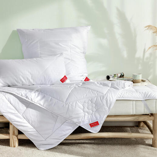 Bett mit weißen Kissen und einer Decke, helle Schlafzimmeratmosphäre.