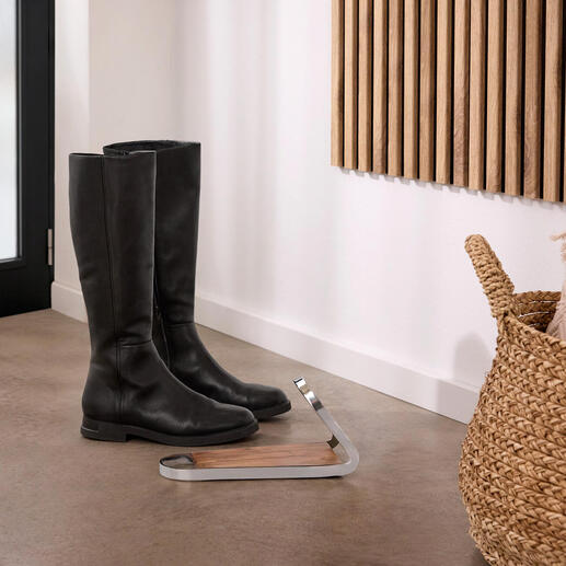 Schwarze Stiefel stehen neben einem modernen Stiefelknecht aus Holz und Metall.