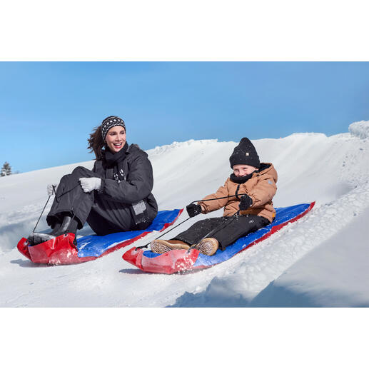 Frau und Kind fahren mit XL-Schneegleitern einen Schneehang hinunter.