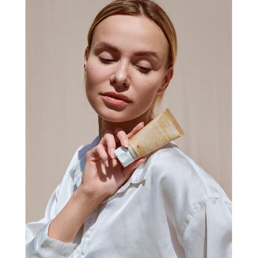 Frau mit geschlossenen Augen hält eine Tube Naturkosmetik in der Hand.