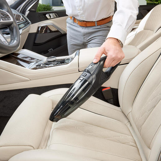 Mann benutzt einen Akku-Handsauger zur Reinigung des Autositzes mit hellem Interieur.