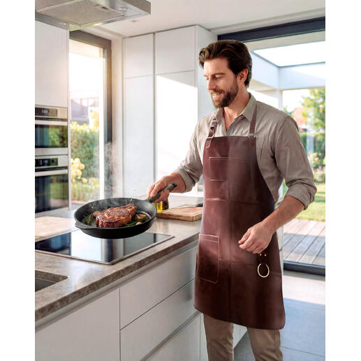 Mann mit Büffelleder-Grillschürze kocht in einer modernen Küche.