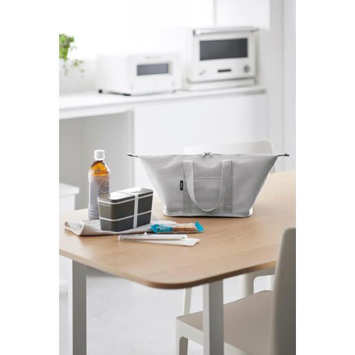 Hellgraue Vario-Kühltasche auf einem Tisch, umgeben von Snacks und Getränken.