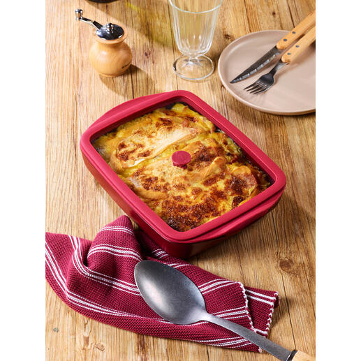 Rote Ofenform mit Deckel, gefüllt mit einer Bohnenspeise, auf einem Holztisch.