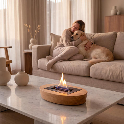 Moderner Eiche-Tischkamin mit Flamme, Frau entspannt neben einem Hund auf der Couch.