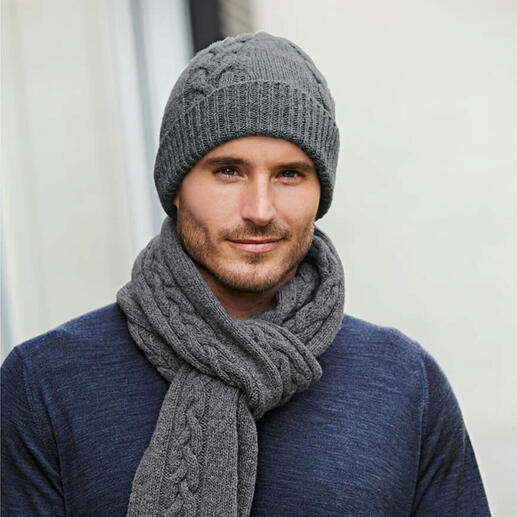 Mann in grauer Zopfstrick-Mütze und -Schal, trägt einen blauen Pullover.